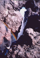 Rainbow formed by waves crashing underneath a rock outcrop that went out over the ocean.